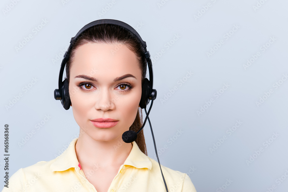 Portrait of a cute brunette call centre operator in a headset. She is isolated on a pure light background, looking serious Portrait of a cute brunette call centre operator in a headset. She is isolated on a pure light background, looking serious