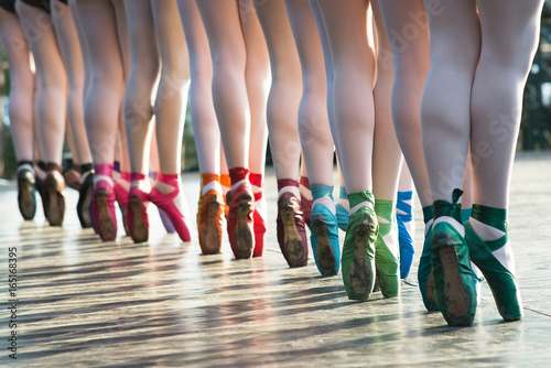 Ballerinas feet dancing on ballet shoes with several colors on stage during a performance.