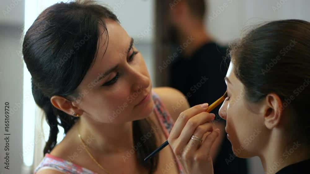 Makeup artist makes models eye evening makeup. Beautiful woman applying shadows on healthy girl's face skin. Slow motion. Close up portrait of ladies in beauty salon. Makeup artist makes models eye evening makeup. Beautiful woman applying shadows on healthy girl's face skin. Slow motion. Close up portrait of ladies in beauty salon.