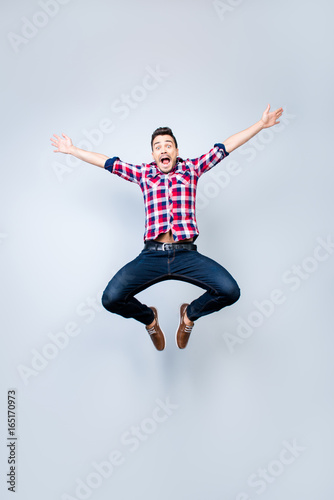Freedom, crazy, funky, carefree, summer mood. Excited brunete guy is jumping and fooling around. He is in casual outfit on light background