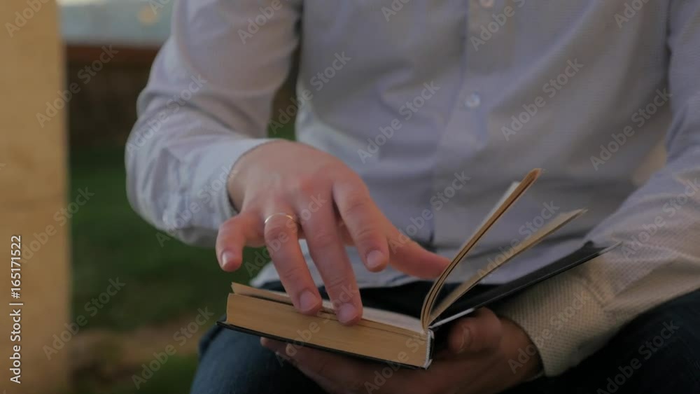 Handsome boy sitting in the park on sunny day and reading book, steadycam shot. Men reading a book on a park bench in a sunny day. Young boy read book in the city. Book's page turning. Handsome boy sitting in the park on sunny day and reading book, steadycam shot. Men reading a book on a park bench in a sunny day. Young boy read book in the city. Book's page turning.