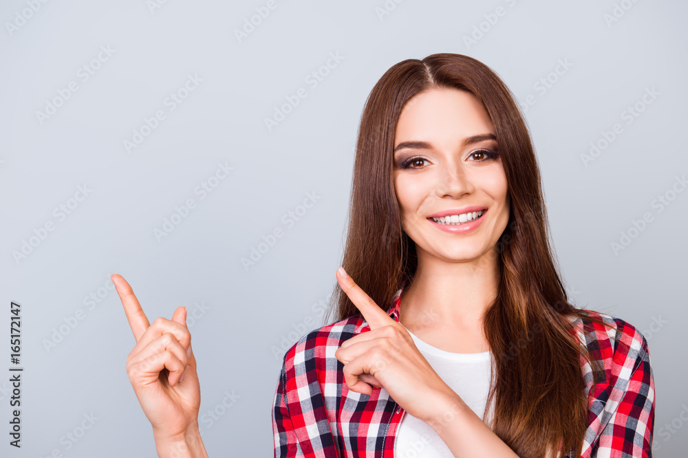 Close up of young brunette girl on the pure light blue background, she is smiling, wearing casual outfit and is pointing on a copyspace with her fingers Close up of young brunette girl on the pure light blue background, she is smiling, wearing casual outfit and is pointing on a copyspace with her fingers