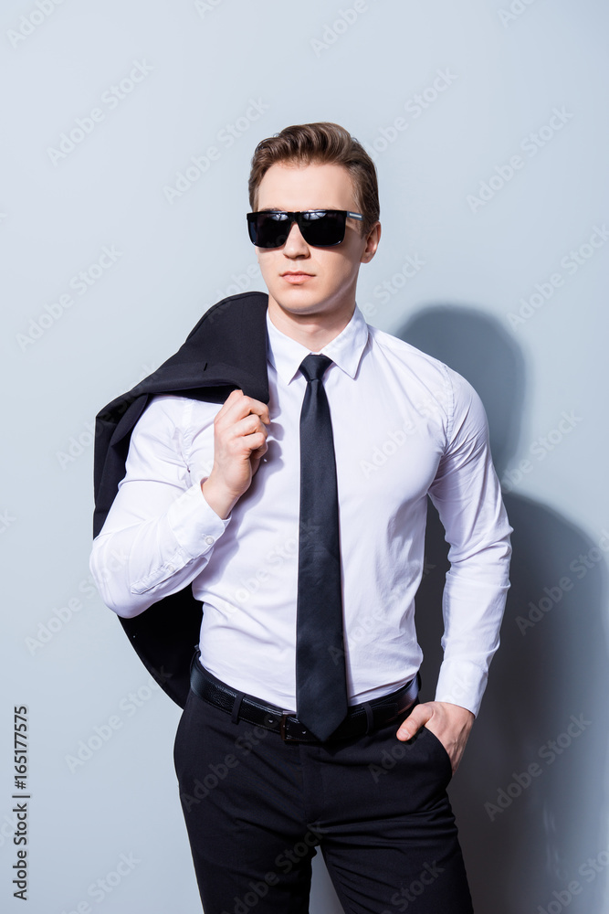 Harsh agent, standing on a pure background. He looks stunning and severe, wearing formal clothes and sunglasses, holds jacket and has a hand in a pocket Harsh agent, standing on a pure background. He looks stunning and severe, wearing formal clothes and sunglasses, holds jacket and has a hand in a pocket