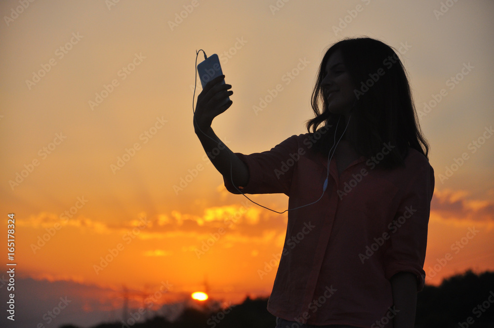 Silhouette of Young Attractive Hipster Girl Listening Music On The Mobile Phone And Dance At Sunset