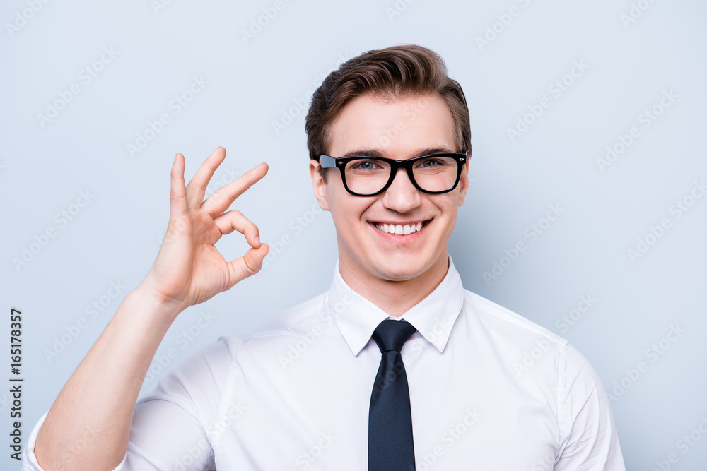 Success concept. Young handsome geek in a formal wear, black glasses, stands on pure light background, gesturing ok sign Success concept. Young handsome geek in a formal wear, black glasses, stands on pure light background, gesturing ok sign