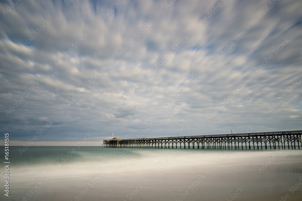 very long wooden pier leading out into the Atlantic Ocean with a sandy beach in the foreground in the summer in South Carolina