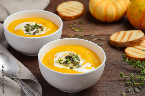 Pumpkin cream soup with cream and pumpkin seeds on wooden background