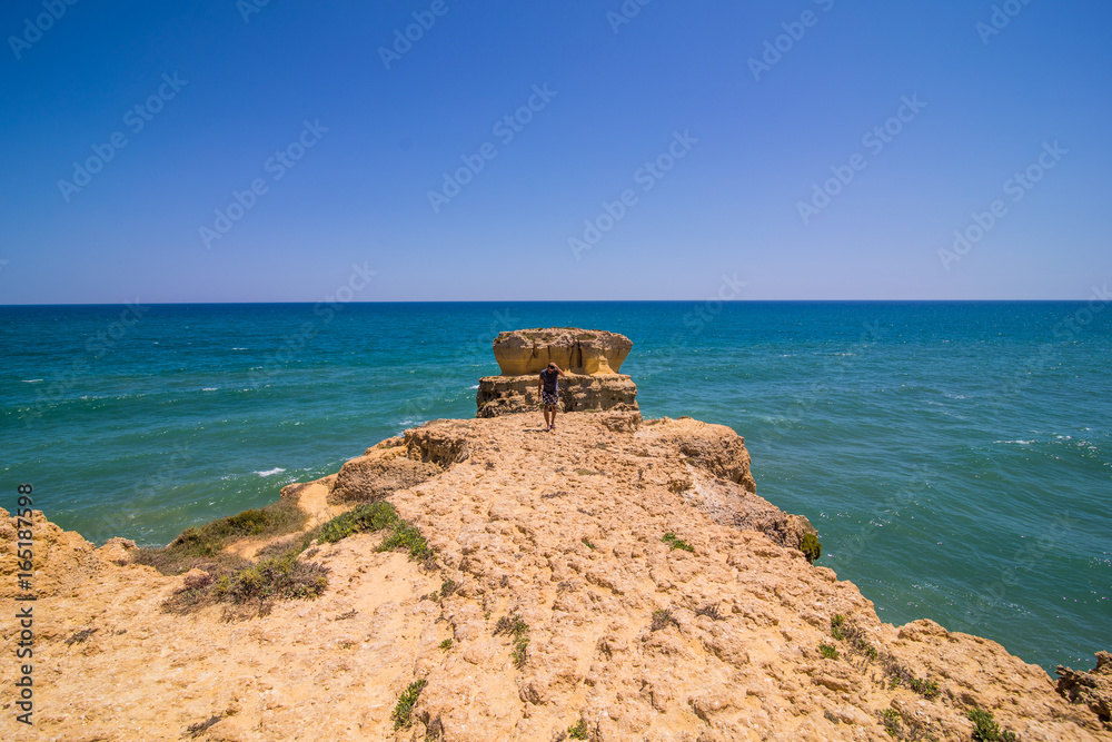 Man walking and enjoy the view of atlantic ocean at the beach with rocks and cliffs at the algarve portugal. summer vocation concept