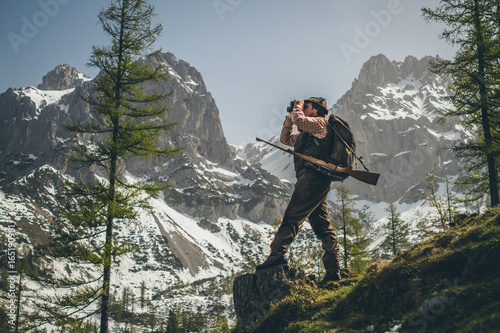 hunter standing on a trunk with his shotgun looking through binocular photo