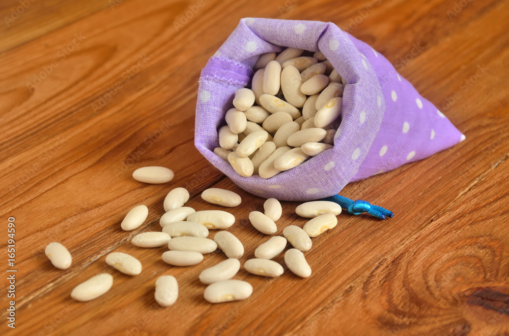 Beans are scattered on the wooden surface of a small fabric bag