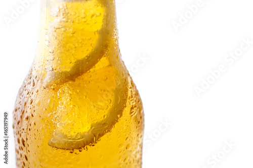 Close up of a bottle of blonde beer with lemon inside and white background
