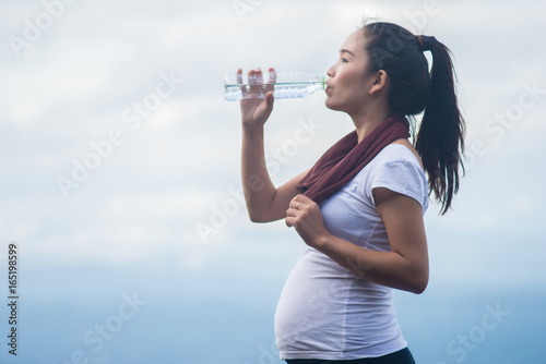 woman drinking a bottle of water on top of mountain.