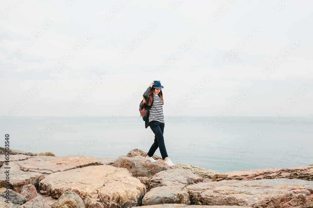 Fototapeta premium A traveler in a hat with a backpack walks next to the sea. Travel, tourism, freedom.