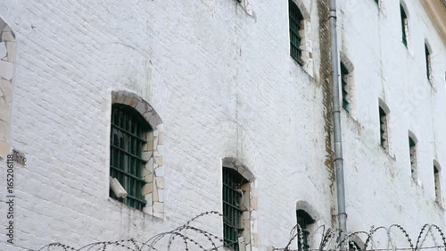 Fence with barbed wire and white prison building, close-up photo