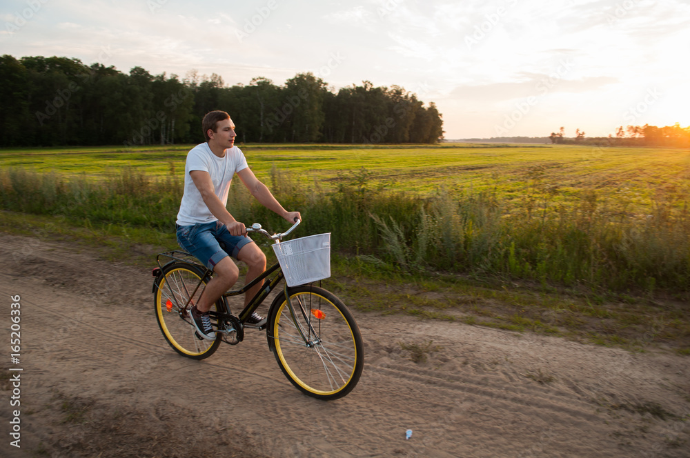 Obraz premium The guy rides a Bicycle along a country road at sunset,