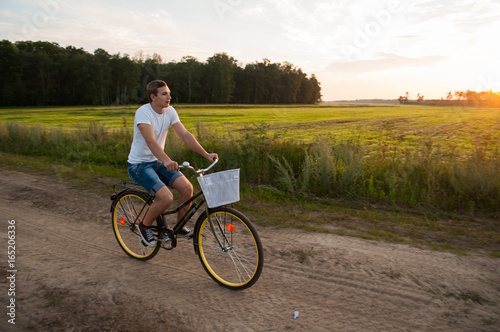 The guy rides a Bicycle along a country road at sunset,