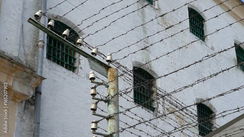 Windows of prison cells behind a fence with barbed wire under high voltage, close-up photo