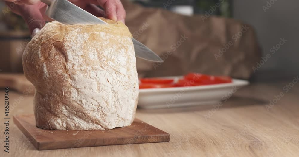 Slow motion slide shot of young man hands cutting ciabatta bread for making sandwich