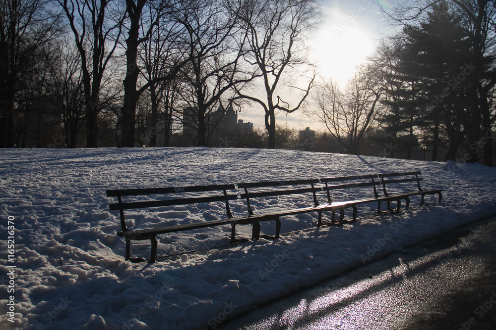 Park benches on snow with sunset at Central Park