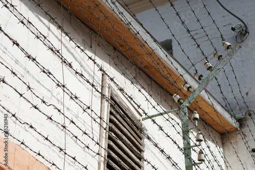 Windows of prison cells behind a fence with barbed wire under high voltage, close-up photo