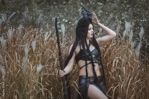 Girl-savage with horns stands in the thickets and looks into the distance photo