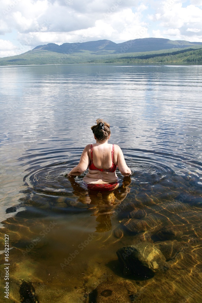 Overweight woman entering a mountain lake to take a swim Overweight woman entering a mountain lake to take a swim