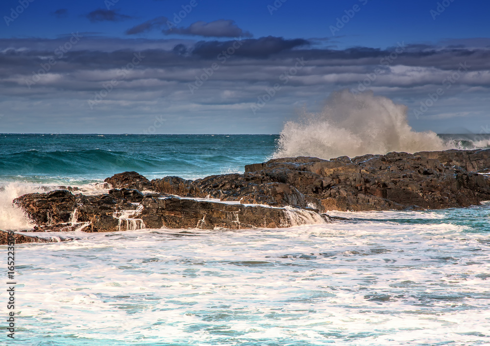 Waves breaking at rocks of the Indian Ocean at the Wild Coast of South Africa with cloudy sky