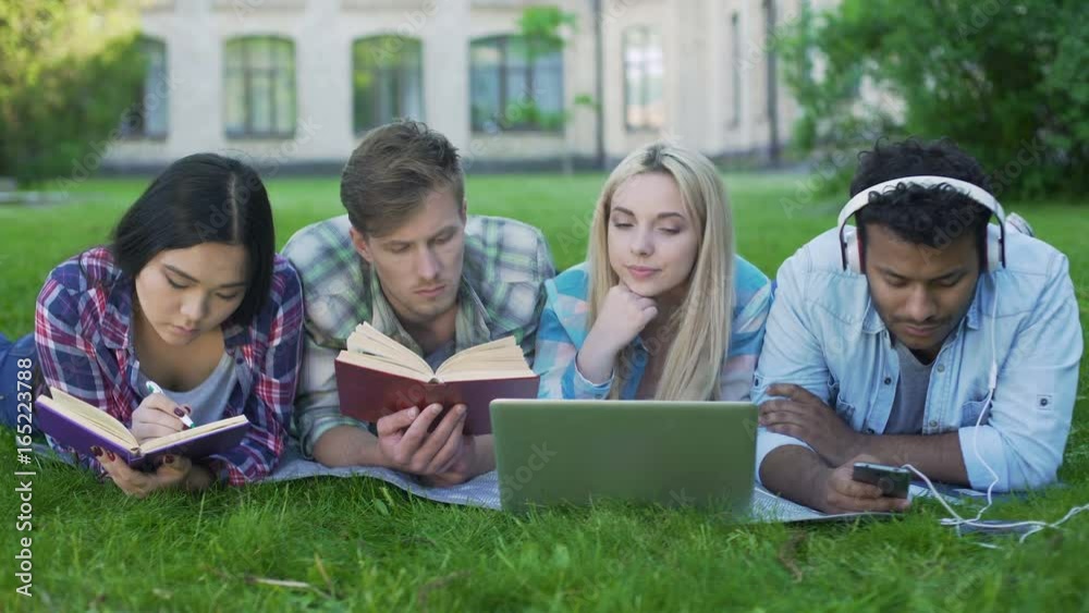 Multi-ethnic men and women doing homework on grass on campus, higher education Multi-ethnic men and women doing homework on grass on campus, higher education