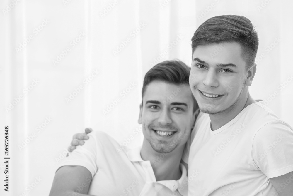 Happy gay couple sitting against window