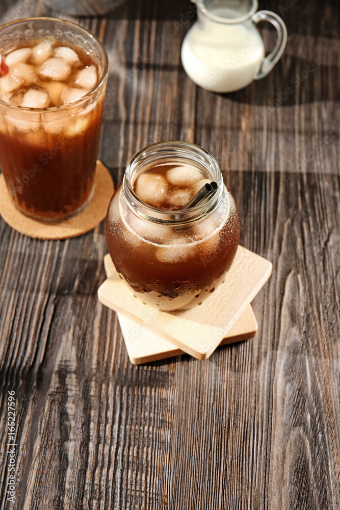 Jar and glass with cold brew coffee on wooden table