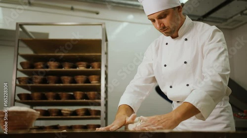 Portrait of baker kneading dough in flour on table fot the future loafs of bread in the modern bakery background. View from the bottom. photo