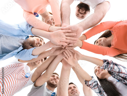 Group of young volunteers standing in circle and holding their hands together on white background