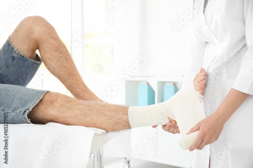 Doctor applying bandage onto patient's leg in clinic
