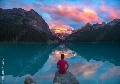 Man in red sit on rock watching Lake Louise morning clouds with reflections photo