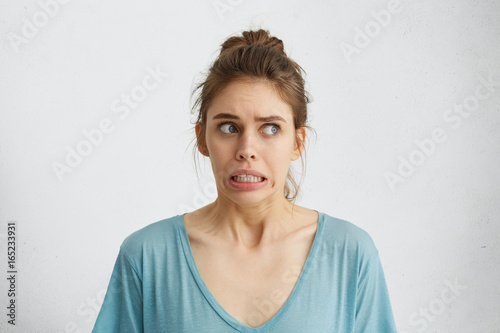 Beautiful woman in casual clothes looking nervously aside feeling distrust or fear while posing against white background. Scared blue-eyed female holding her breath with anticipation of horror