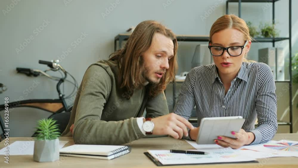 Business partner working in the office, young woman using the tablet for showing the report to his partner. Business partner working in the office, young woman using the tablet for showing the report to his partner.