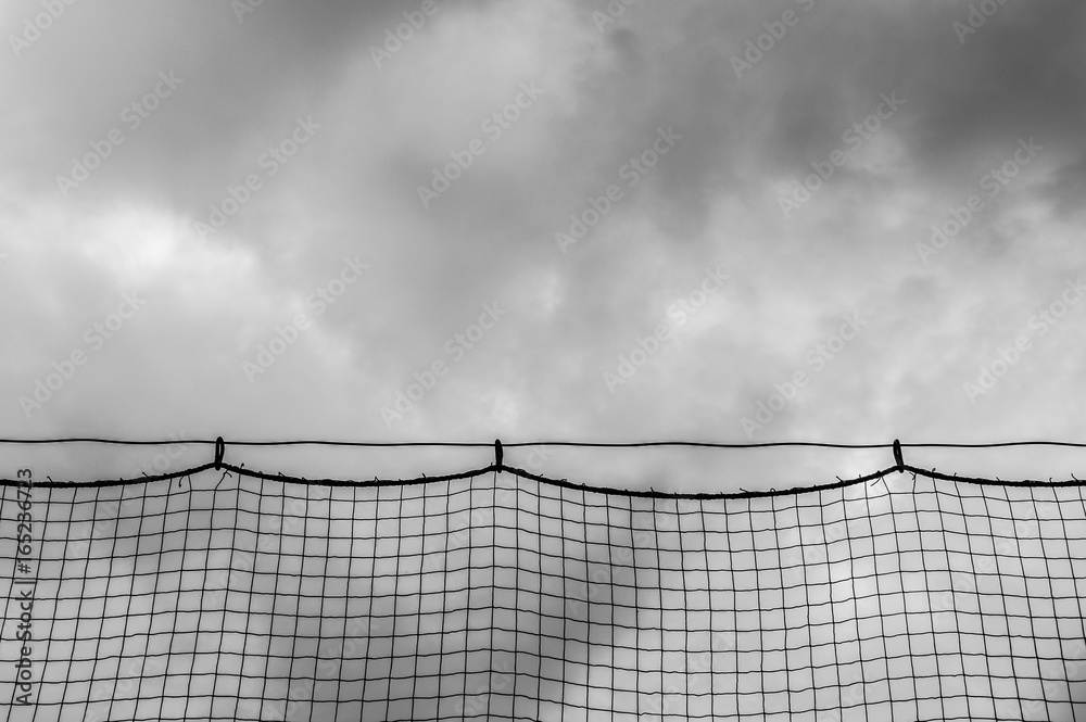dark ominous storm clouds through netting at a baseball field dark ominous storm clouds through netting at a baseball field