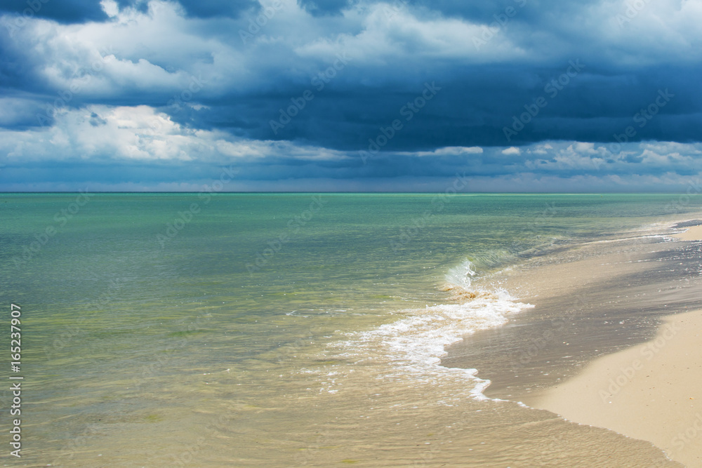 Seaside with waves and dark clouds over water.