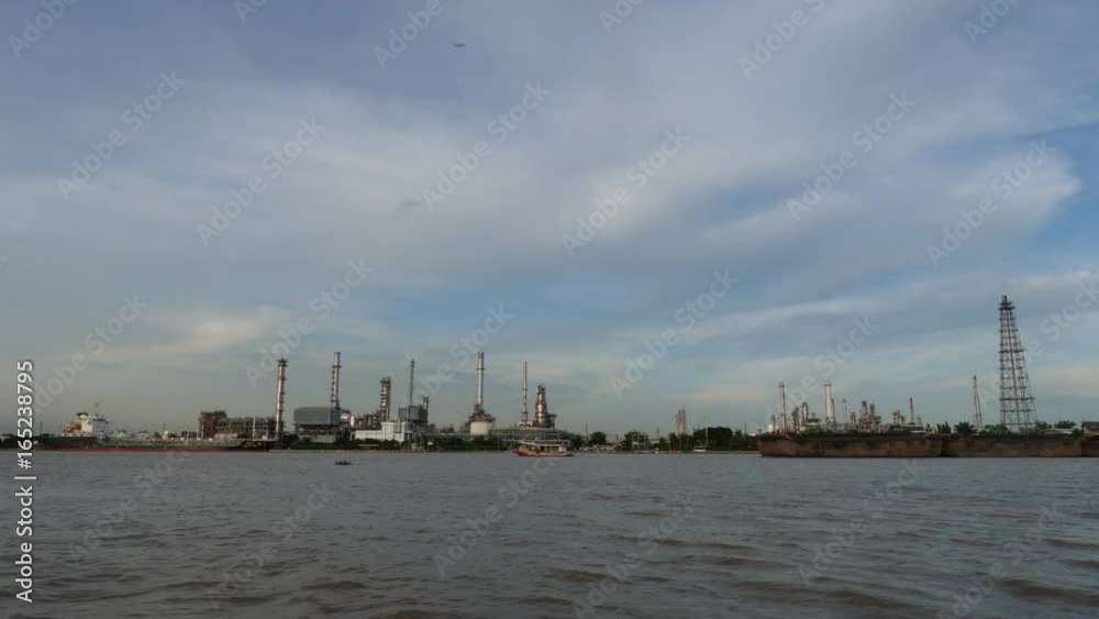 Time lapse. Cargo container ship, Carrier boat floating and moving in river with Oil Petrochemical energy plant background. Business Industry and Logistics shipping, maritime transportation concept Time lapse. Cargo container ship, Carrier boat floating and moving in river with Oil Petrochemical energy plant background. Business Industry and Logistics shipping, maritime transportation concept