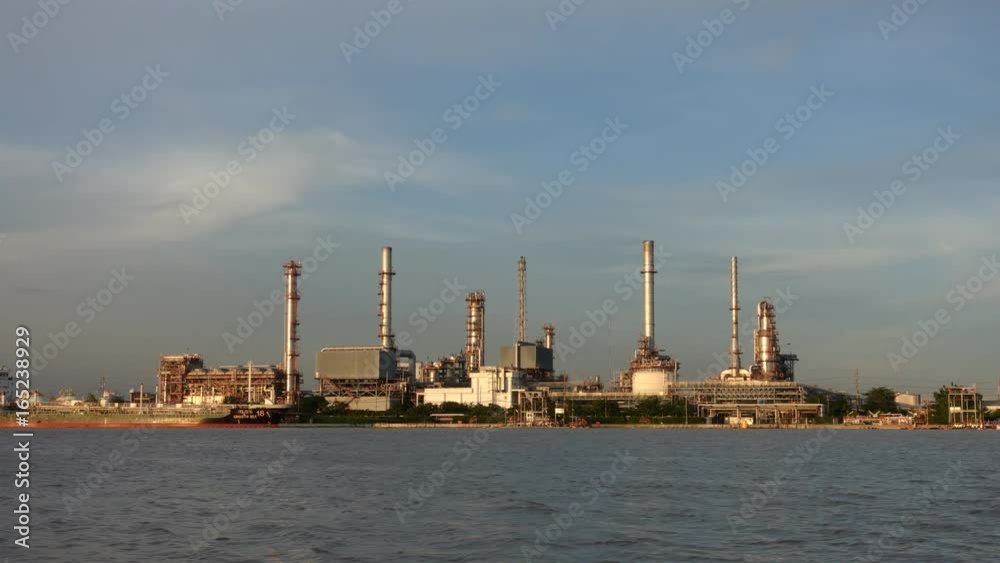 Time lapse. Cargo container ship, Carrier boat floating and moving in river with Oil Petrochemical energy plant background. Business Industry and Logistics shipping, maritime transportation concept Time lapse. Cargo container ship, Carrier boat floating and moving in river with Oil Petrochemical energy plant background. Business Industry and Logistics shipping, maritime transportation concept