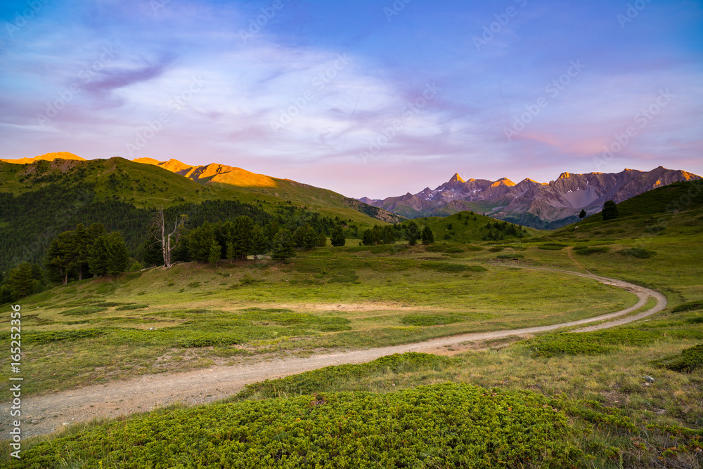 Dirt mountain road leading to high mountain pass in Italy. Expasive view at sunset, colorful dramatic sky, adventures in summer time, Italian Alps. Dirt mountain road leading to high mountain pass in Italy. Expasive view at sunset, colorful dramatic sky, adventures in summer time, Italian Alps.