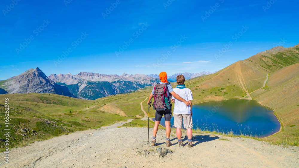 Couple of hiker on the mountain top looking at blue lake and mountain peaks. Summer adventures on the Alps. Wide angle view from above.