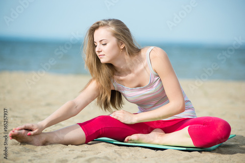 Young lady practicing yoga. Beautiful woman posing at the summer sand beach. Workout near ocean sea coast. Beautiful fit tan girl. Fitness model caucasian ethnicity outdoors. Weight loss exercise
