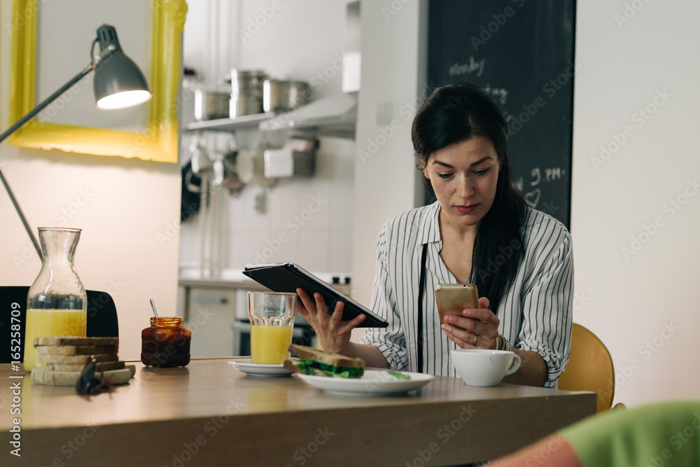 Social media time.young woman having breakfast while using her tablet and mobile phone at her home Social media time.young woman having breakfast while using her tablet and mobile phone at her home