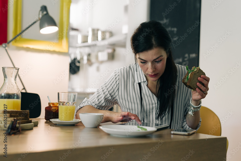 Online leisure time.young woman having breakfast while working on her tablet at home Online leisure time.young woman having breakfast while working on her tablet at home