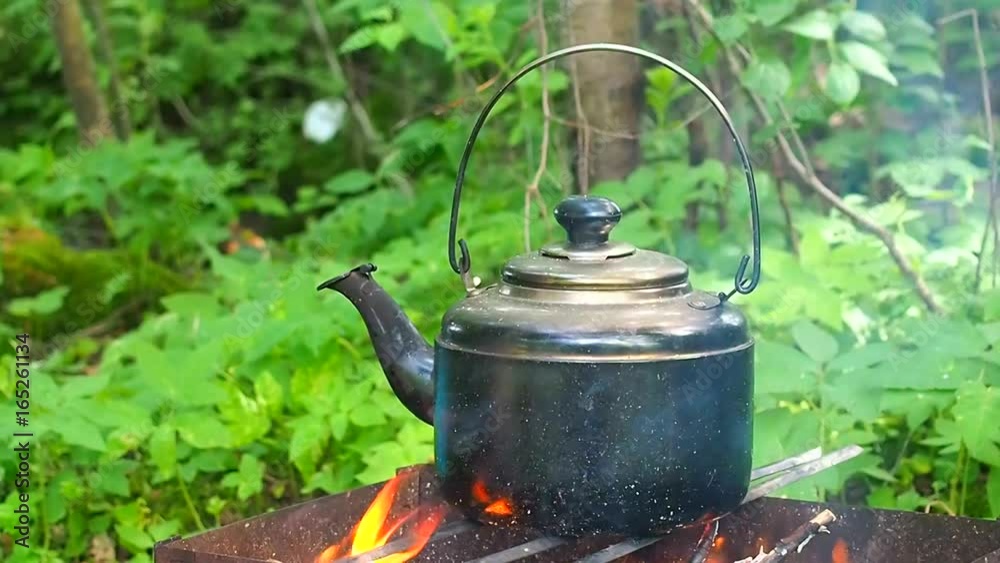 Camping kettle of water on the fire. Food and drink in the campaign for tourists. Tea on the fire in the forest. The romance of travel in nature. Camping kettle of water on the fire. Food and drink in the campaign for tourists. Tea on the fire in the forest. The romance of travel in nature.