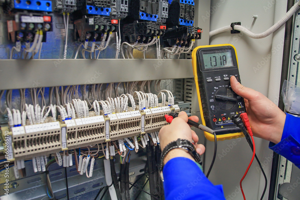 In hands of electrician multimeter on background of electric closet close-up.