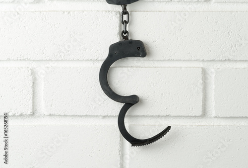 Metal police handcuffs on white painted brick wall