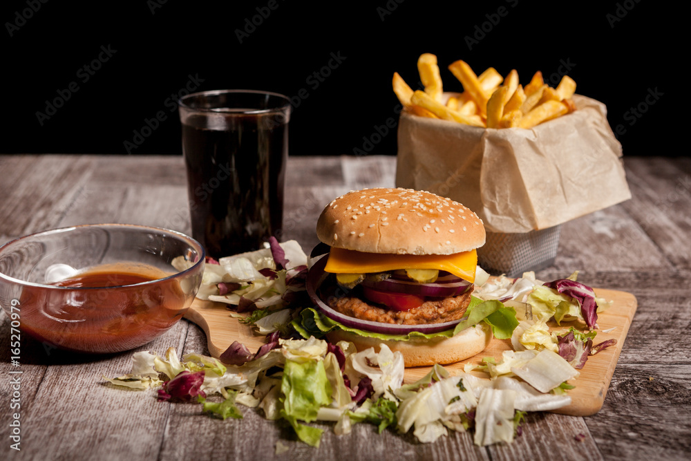 Delicious home made burgers on wooden plate next to a glass of cola and fries. Fast food. Unhealthy snack