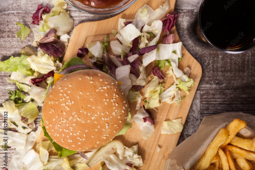 Home made burger on wooden plate next to fries, cola and ketchup. Fast food. Unhealthy snack